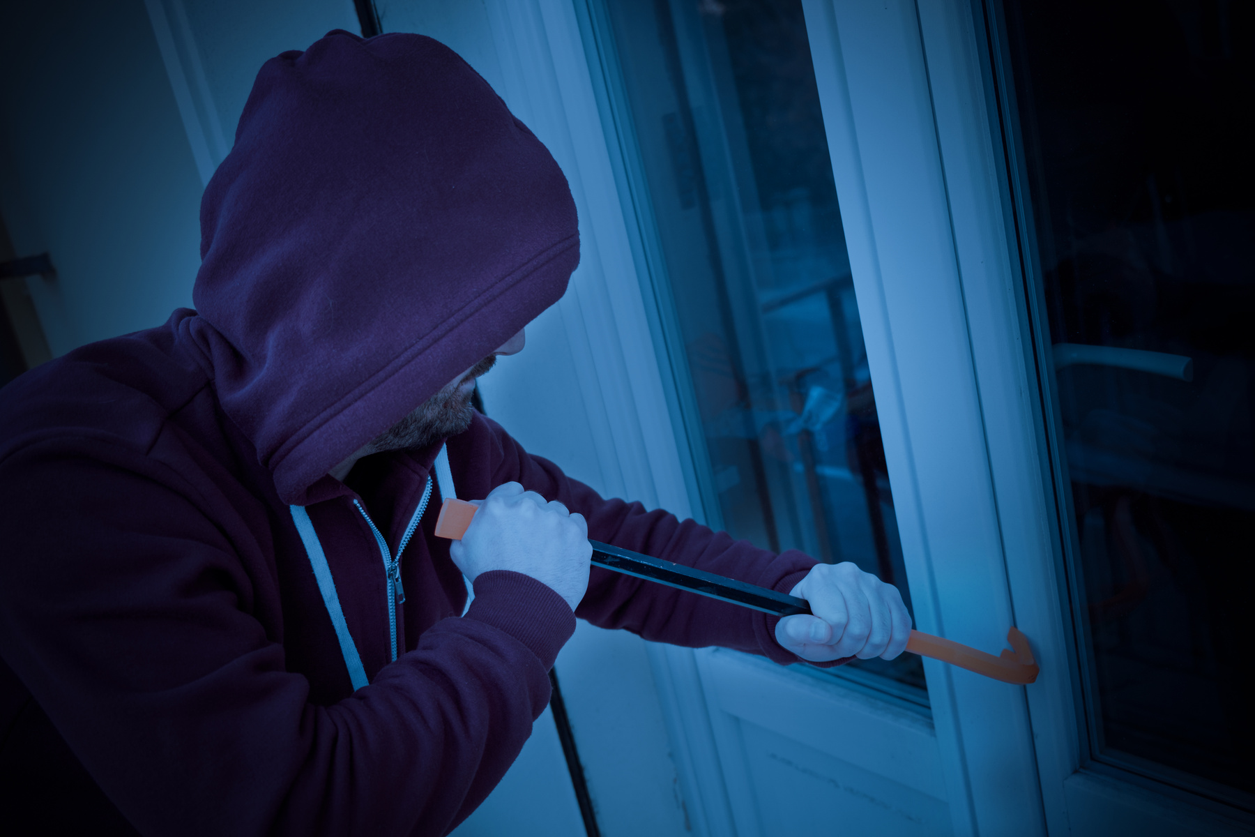 Hooded burglar forcing window to rob in the house